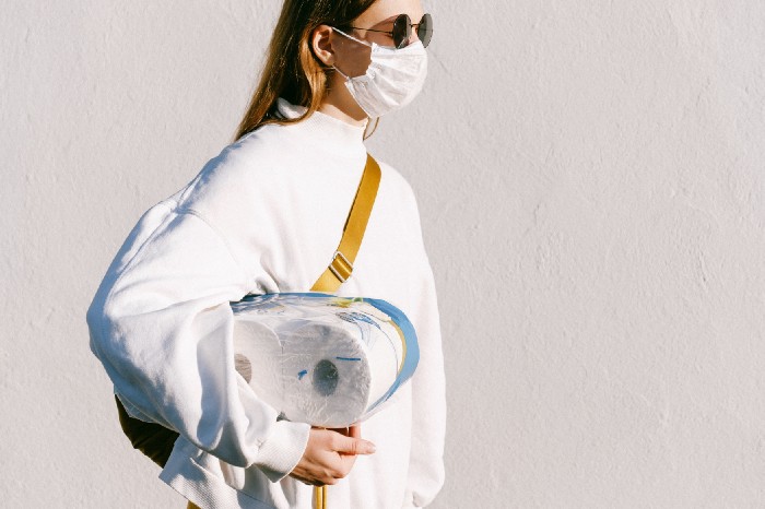 Woman with face mask holding rolls of toilet paper
